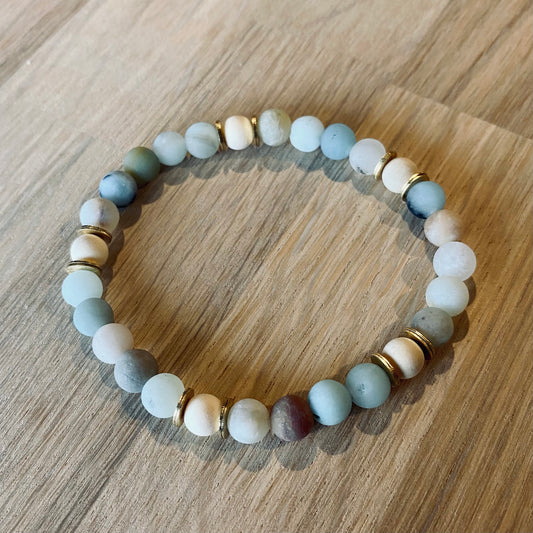 Amazonite aroma bracelet/diffuser bracelet made from 6mm amazonite & natural white wood beads with brass heishi disc embellishments. Laid flat on wood grain surface.
